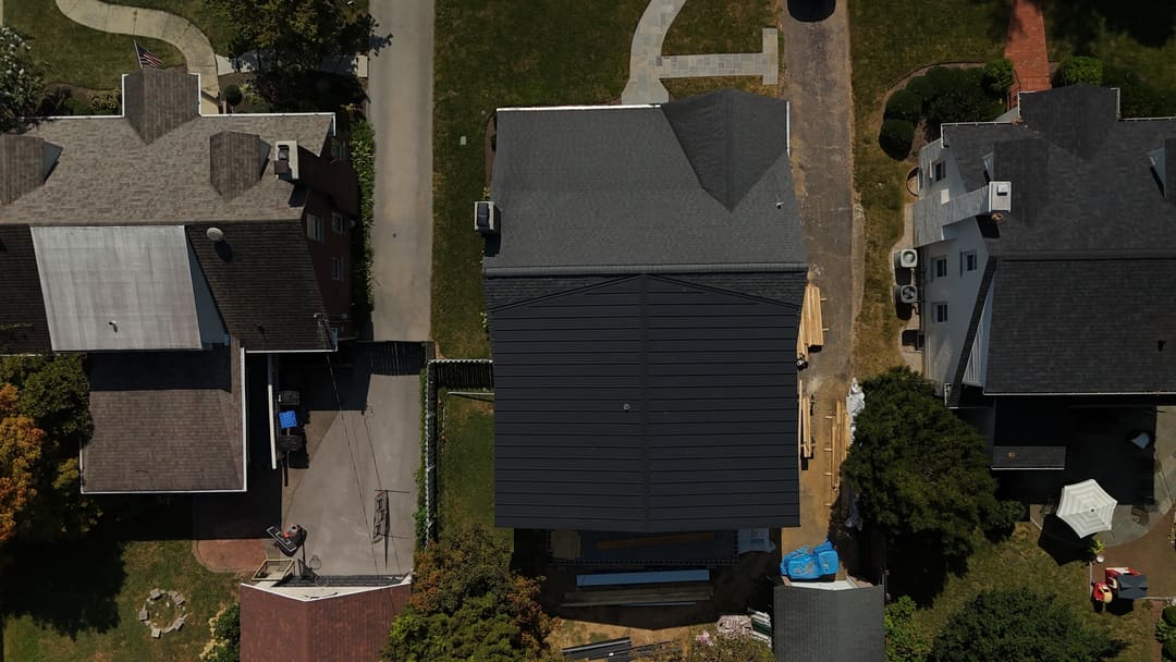 Black metal roof on a two story home between older shingle roofs, seen from above