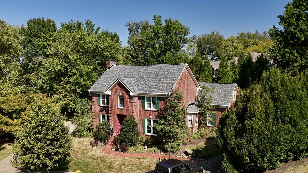Red brick two story home with green shutters and a gray shingle roof, seen from above the front walk