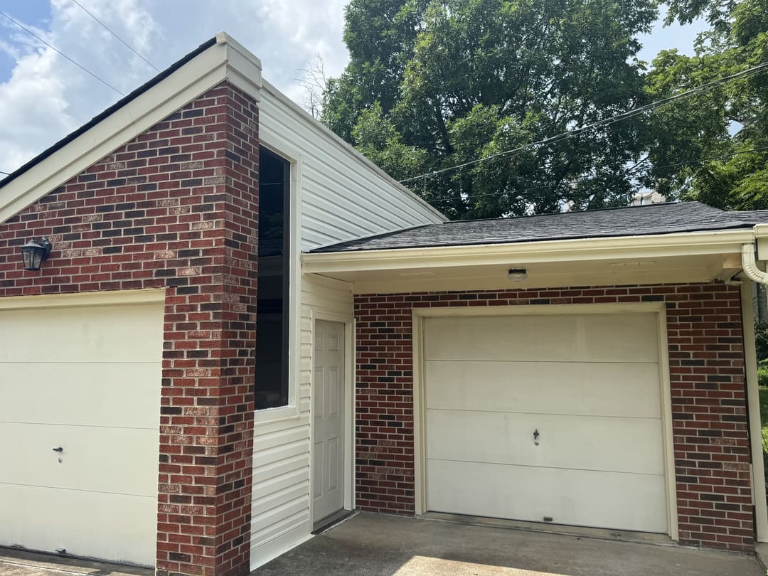 Brick garage with a white overhead door and white siding