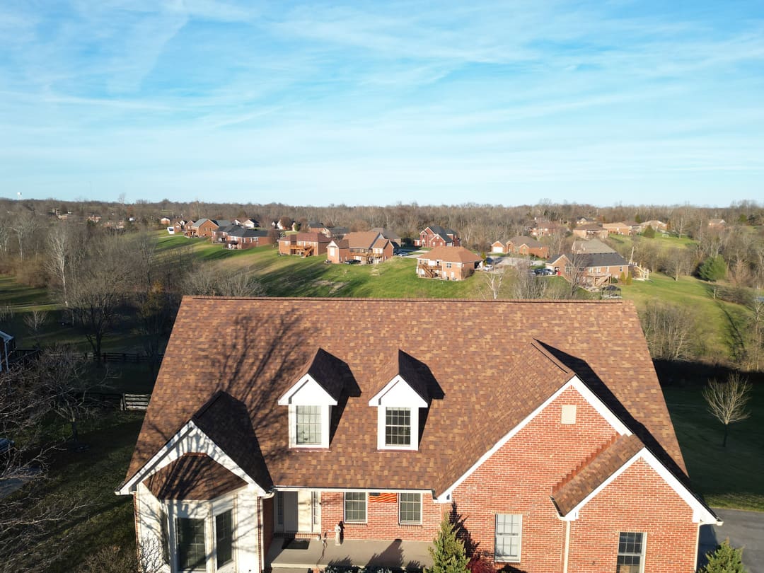 Brown shingle roof and two white dormers on a brick home overlooking a subdivision