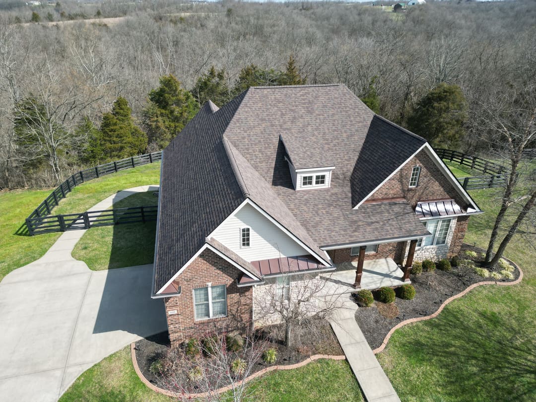 Brown architectural shingle roof with copper porch roofs on a brick and white sided home, seen from above