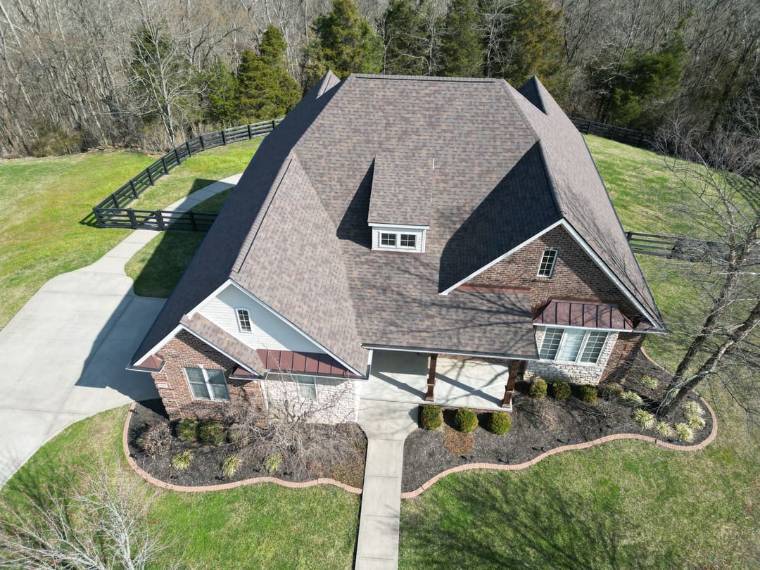 Shingle roof valleys and dormers on a brick home with copper accent roofs and a landscaped drive