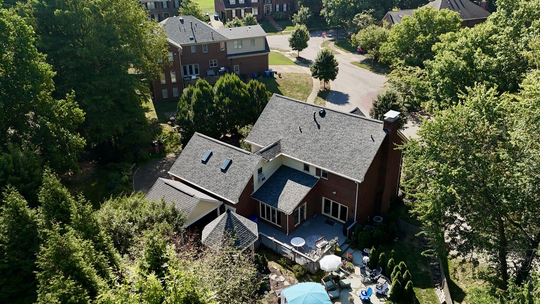 Gray shingle roof with skylights on a large brick home, seen from the air above the back patio