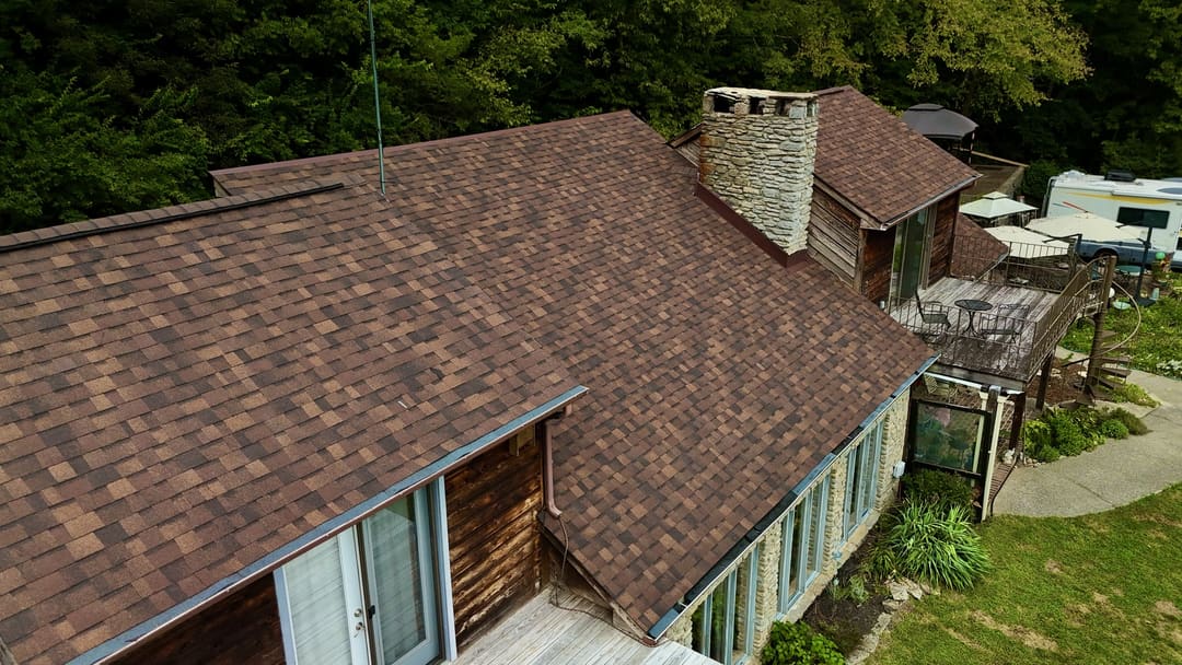 Close aerial of a brown shingle roof meeting a stone chimney