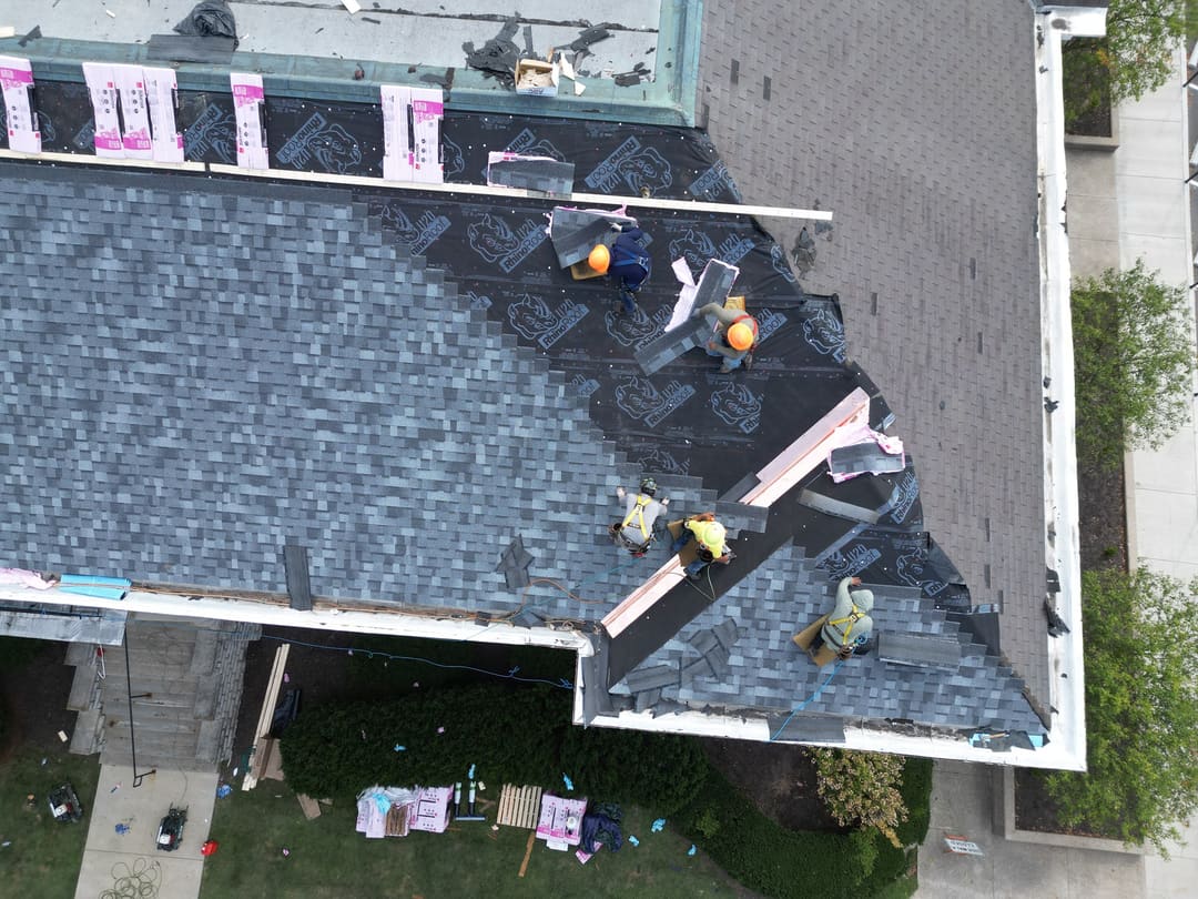 Crew installing new dark shingles on a large roof, seen from straight above