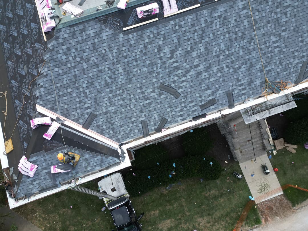 Roofers working down a hip roof with bundles staged on the ridge