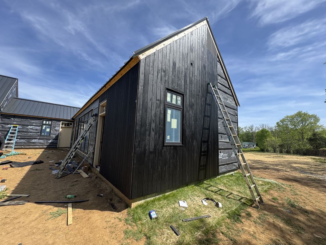 Dark vertical wood siding on a modern gable end, ladders still on site