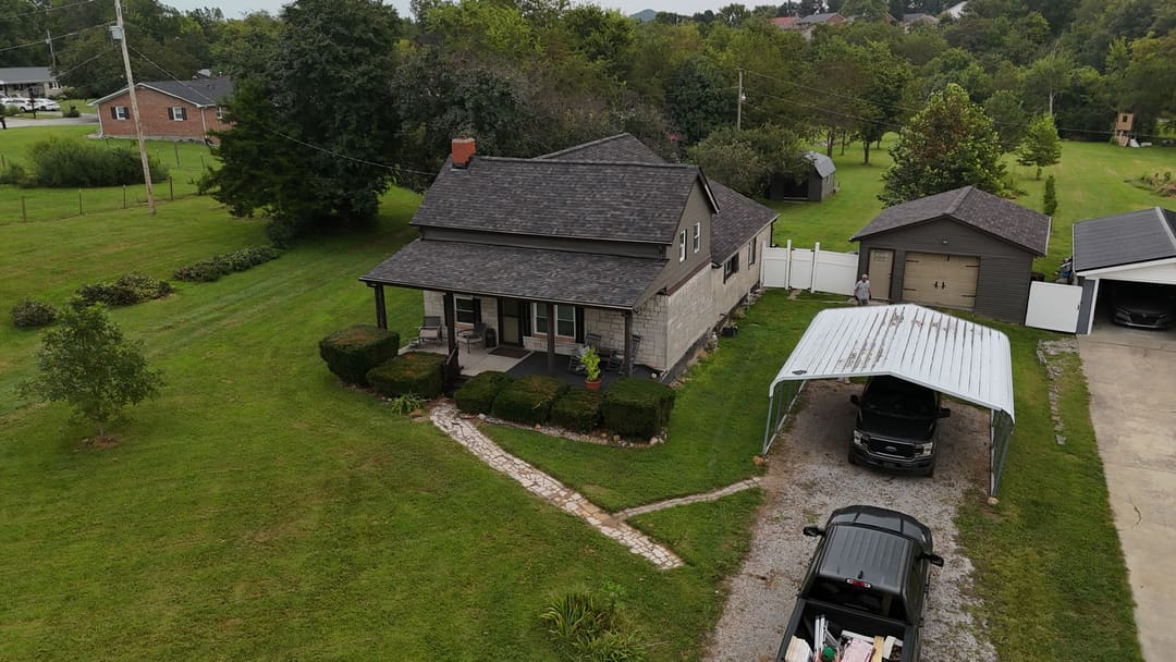 Gray shingle roof on a farmhouse with a metal carport and outbuildings