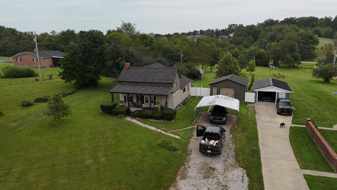 Farmhouse with a new gray roof at the end of a gravel drive