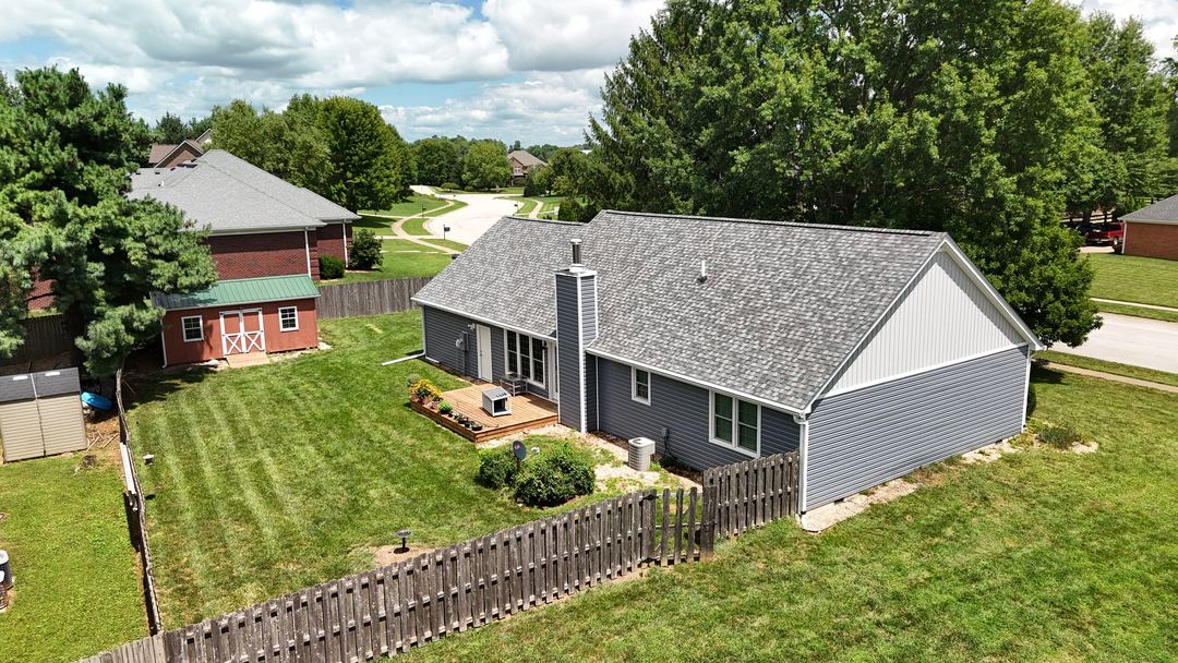 Gray sided home with a shingle roof and a fenced back yard with a red shed, seen from the air