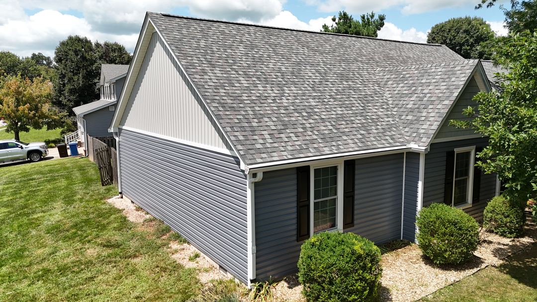 Gray shingle roof above gray vinyl siding, a white gable end and white gutters, seen from the air
