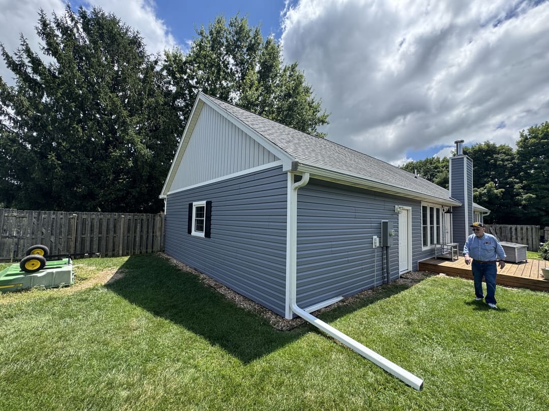 Back of a home in new gray vinyl siding with white board and batten gables