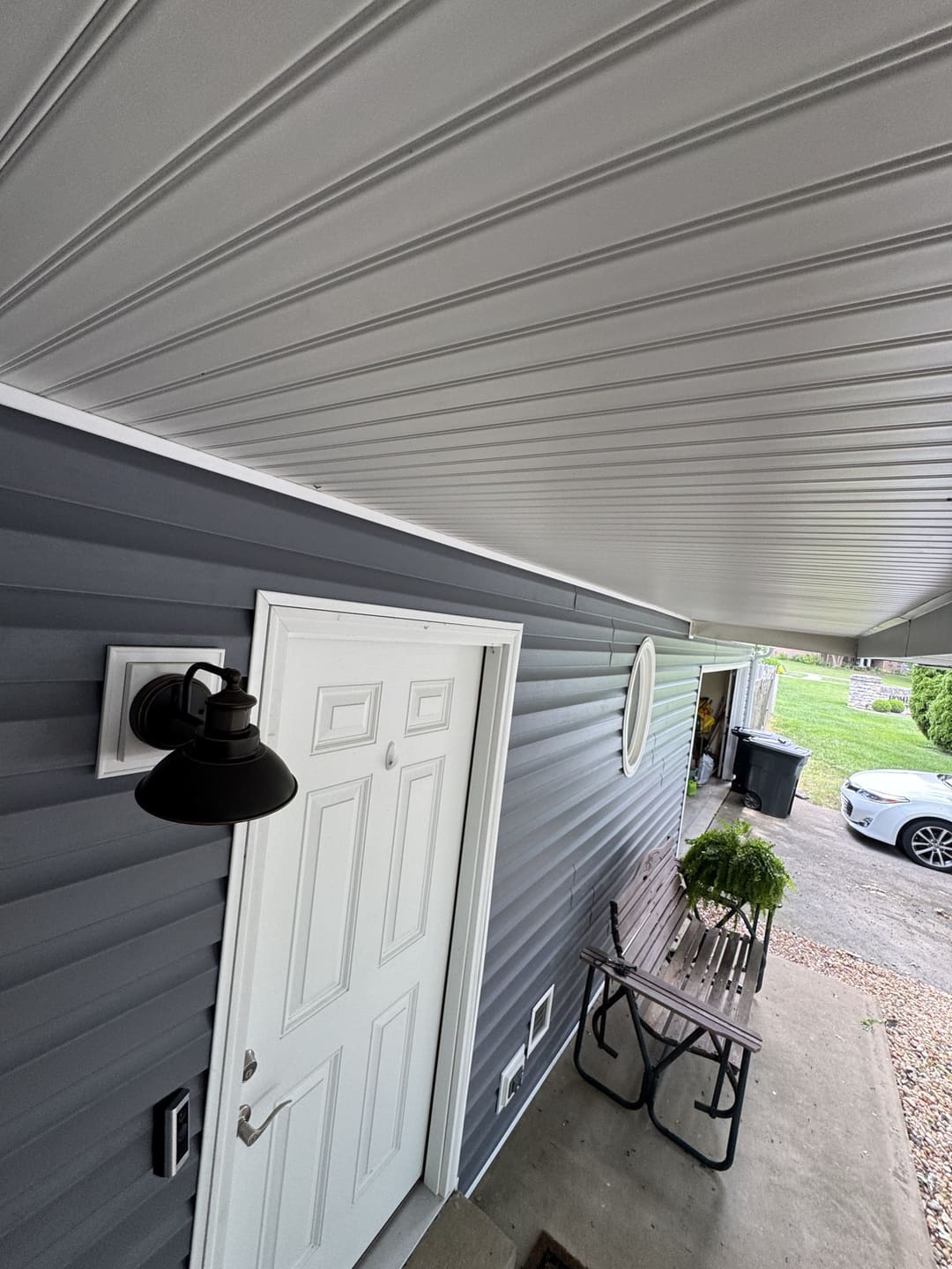 Entry door, lantern and oval window framed in new gray vinyl siding