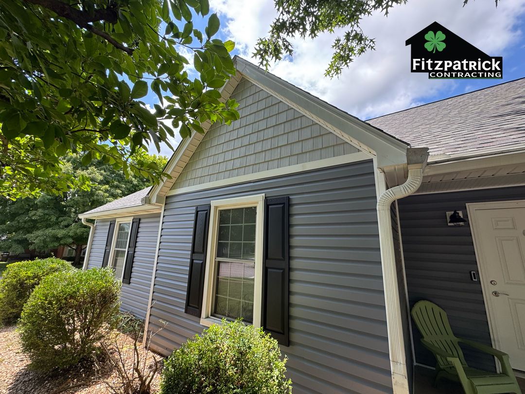 Gray vinyl siding with shake trim in the gable peak, a window in black shutters and the gutter along the eave