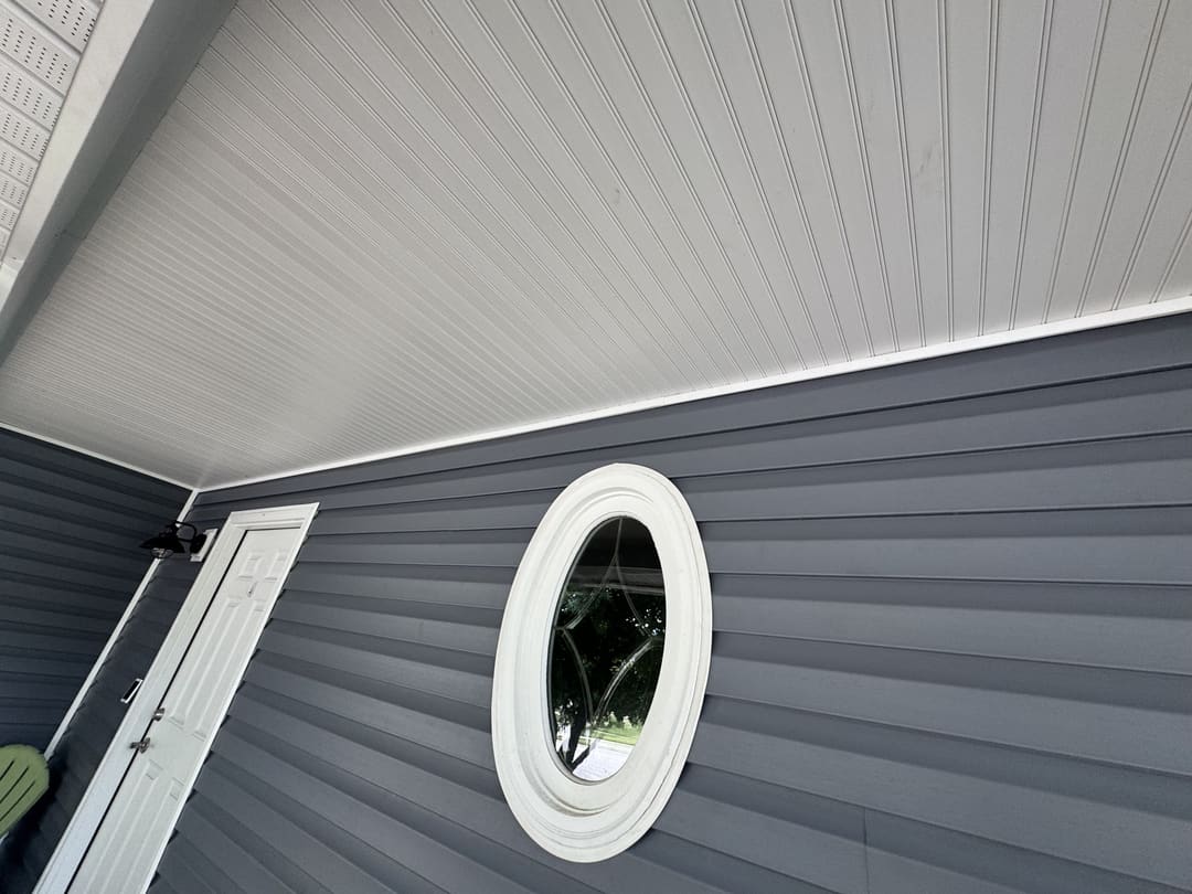 White soffit and an oval window set in new gray vinyl siding
