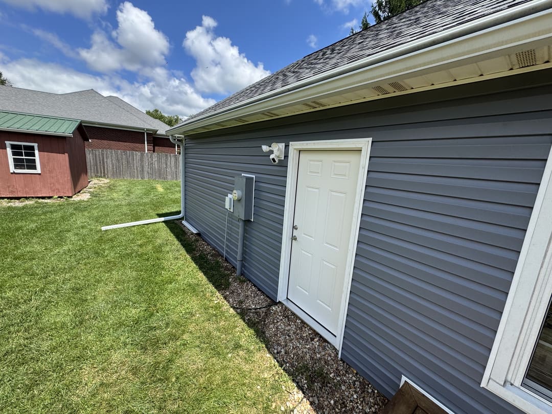 Side of a home in new gray vinyl siding with a white door and downspout