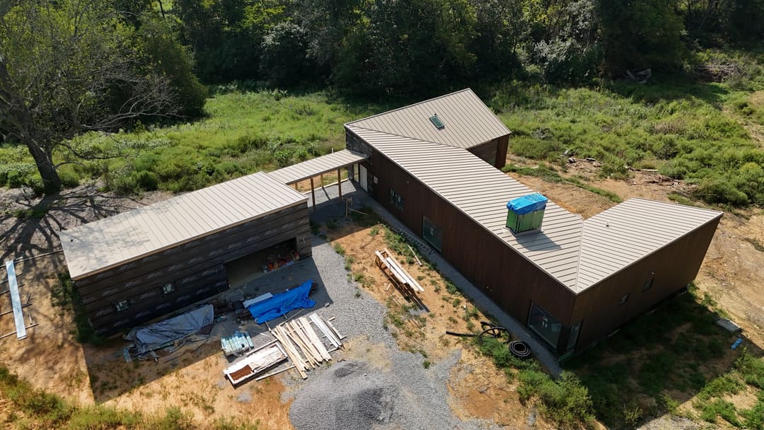 The long wing of a modern home with a tan standing seam roof and dark wood siding