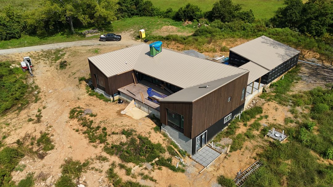 Tan standing seam metal roof on a modern home and its detached wing, seen from the air across the whole site