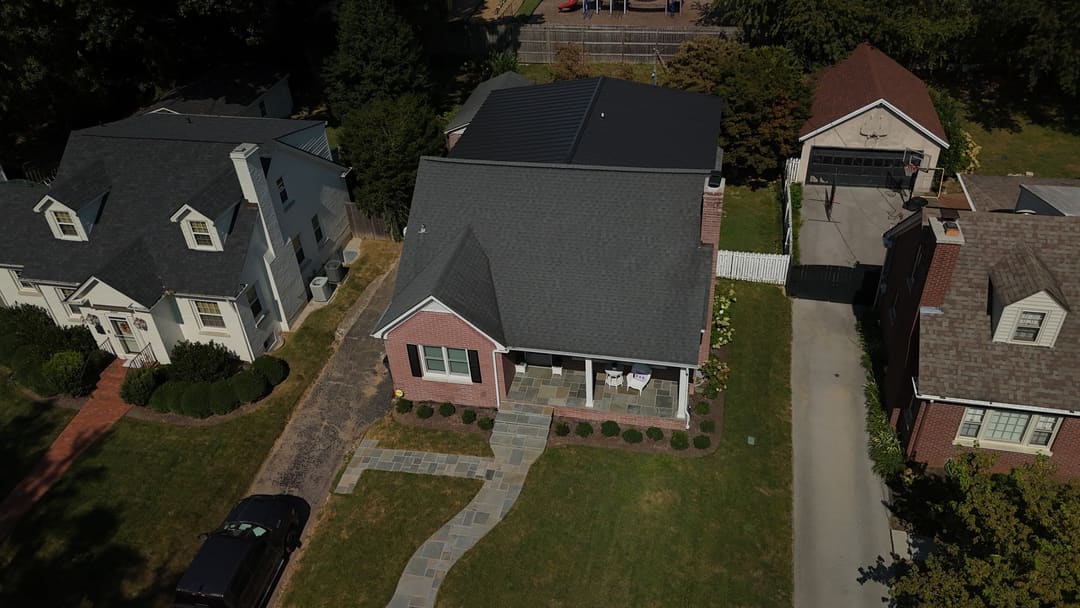 Brick home with a gray shingle roof and a black standing seam roof on the addition behind it, from the street side