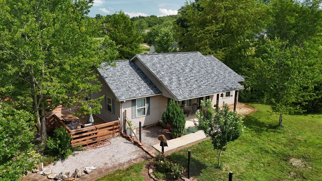 Ranch home with a gray shingle roof and a wood deck, with a wire fence and trees around the yard