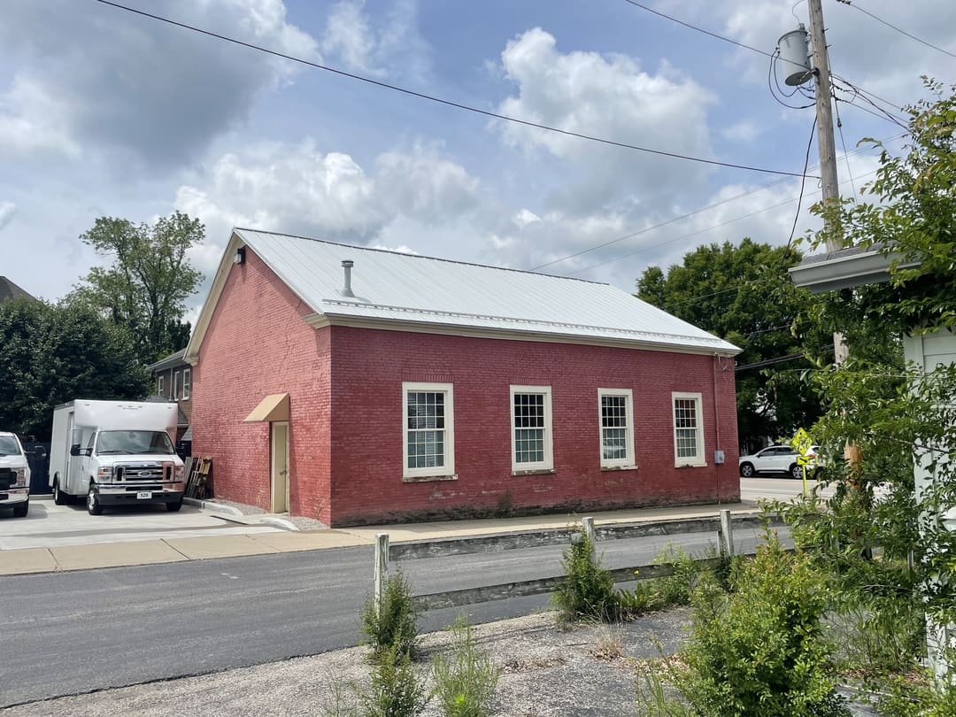 Red brick building with a silver metal roof beside the street