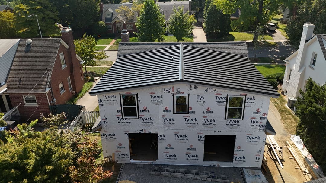 Front of a new build in house wrap with a fresh black standing seam metal roof