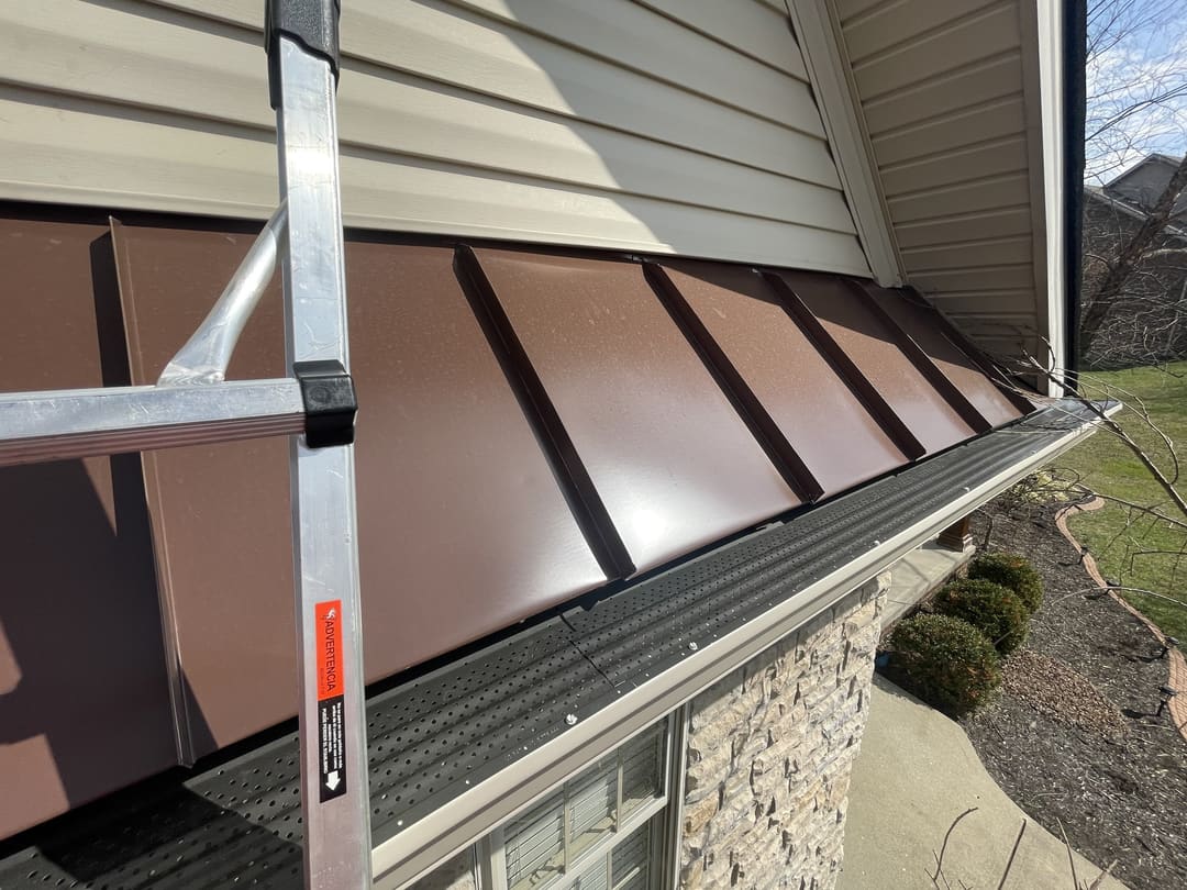 Brown standing seam porch roof and a new gutter along a stone front