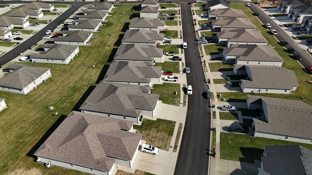 A subdivision street of matching shingle roofs, seen from the drone