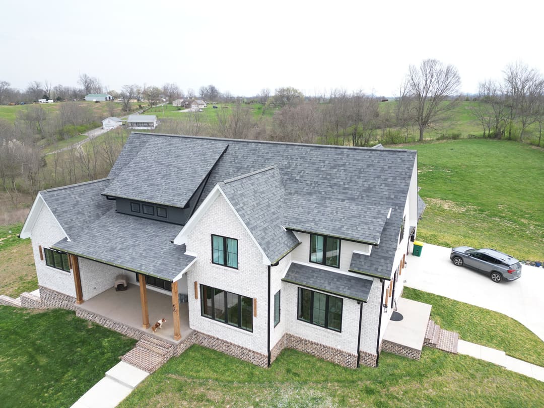 Gray shingle roof on a white modern farmhouse with black windows and a wood porch, seen from the air