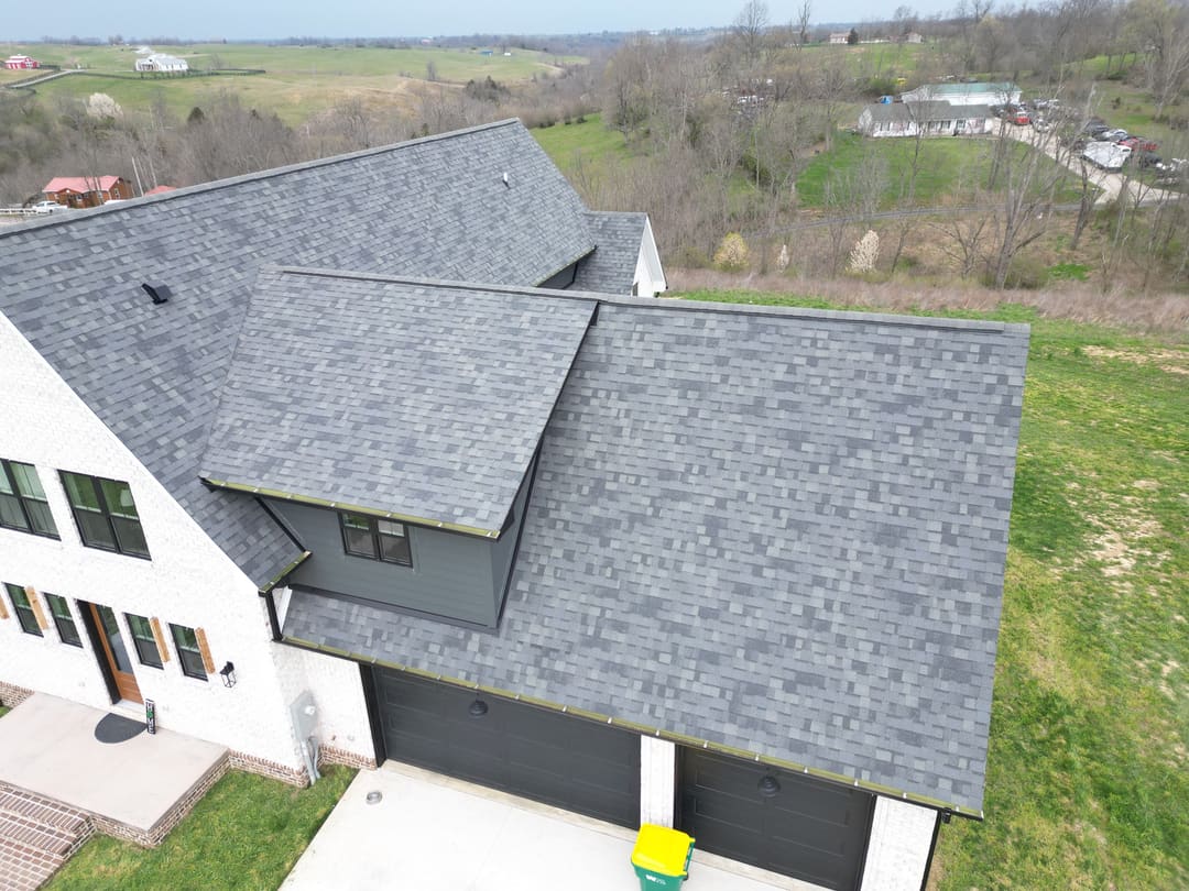 Gray shingle roof over the garage wing of a white farmhouse, with fields behind it